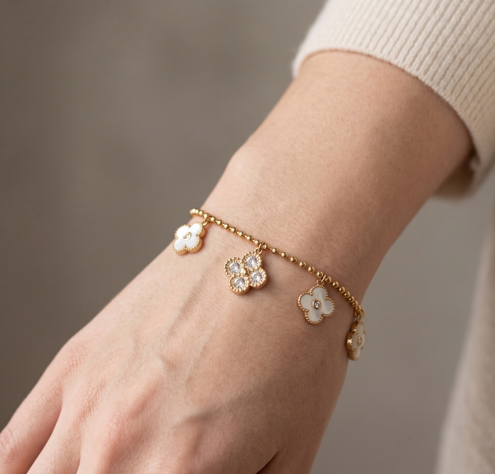 Gold bracelet with floral charms on a wrist against a neutral background