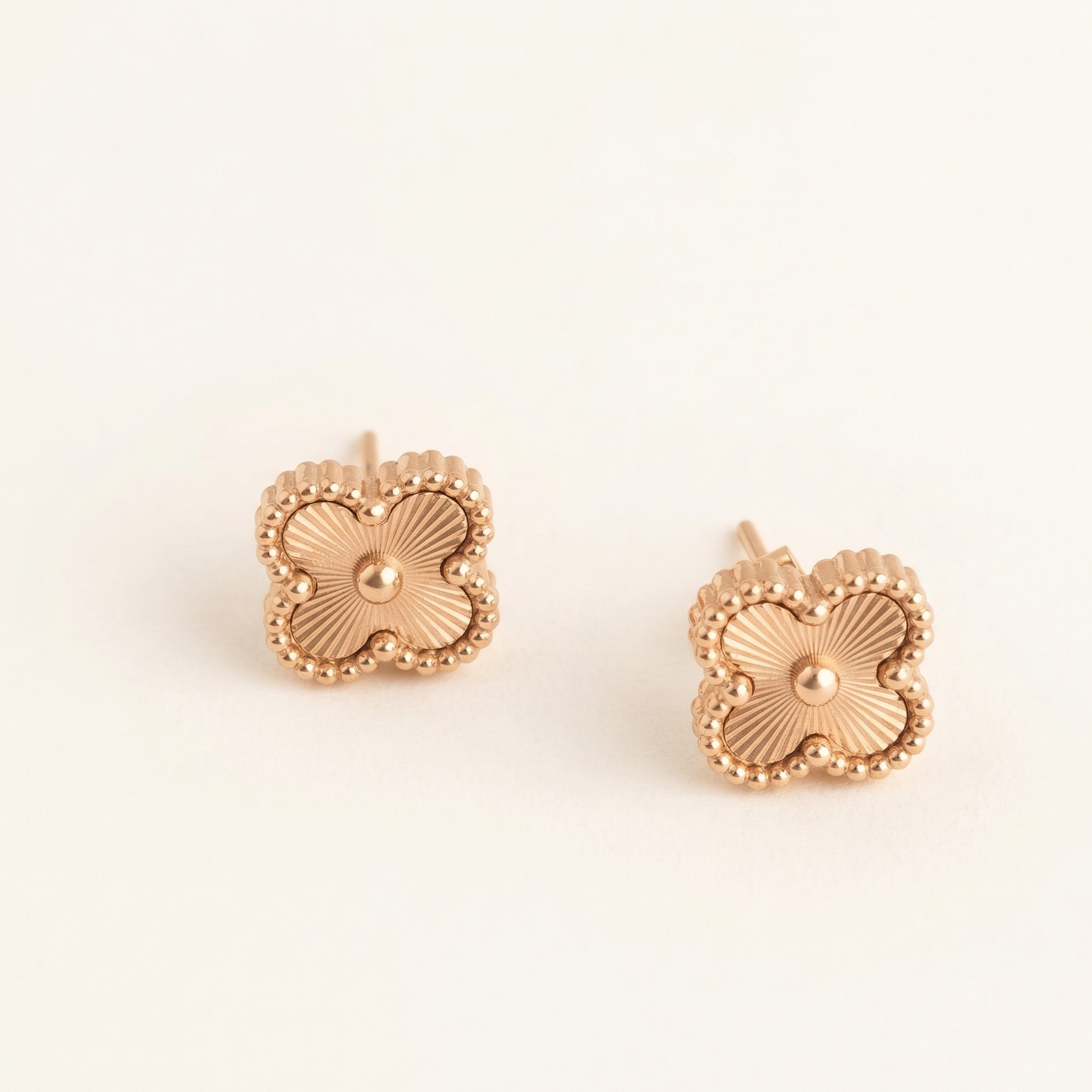 Pair of rose gold floral earrings on a light beige background