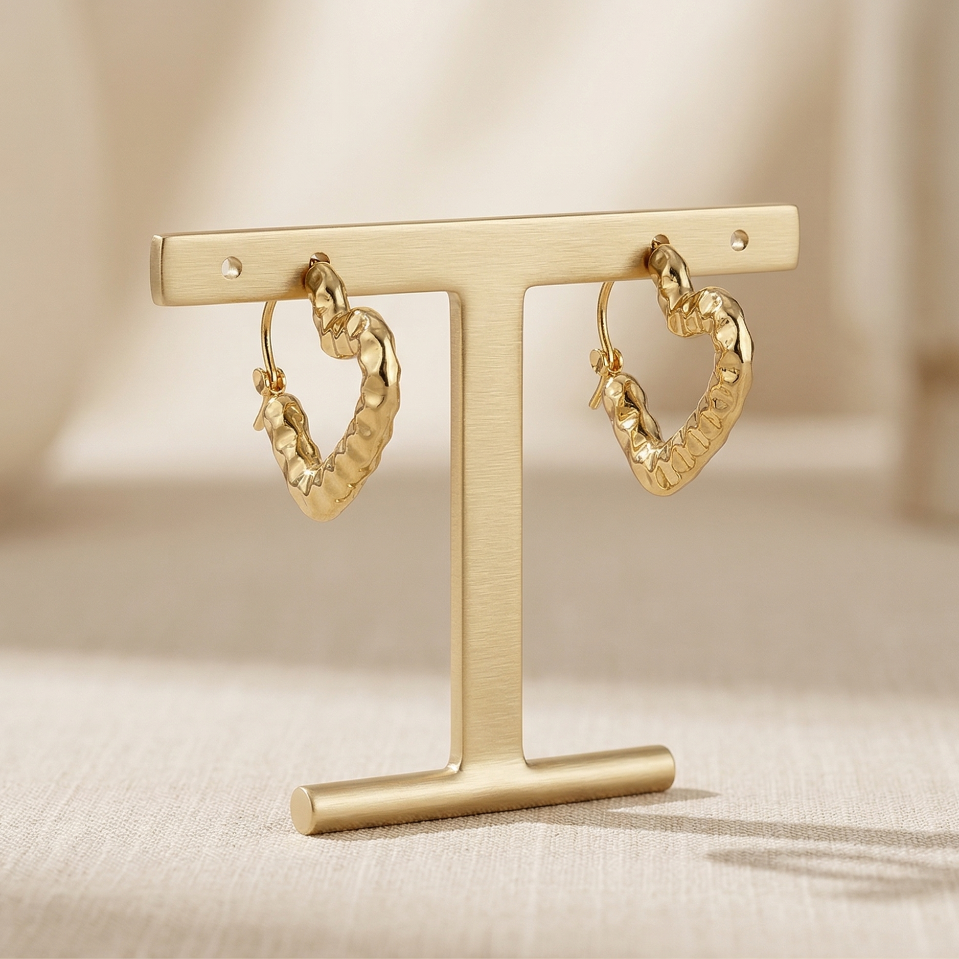 Gold heart-shaped hoop earrings on a gold T-shaped stand against a neutral background