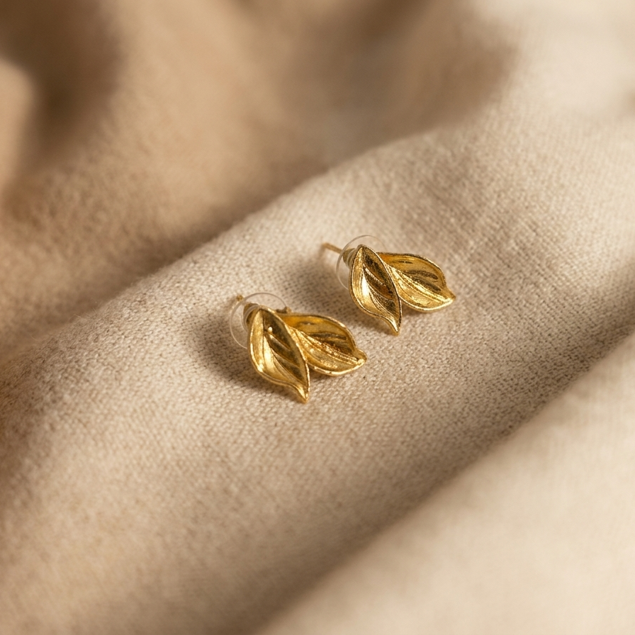 Gold leaf-shaped earrings on a beige fabric background