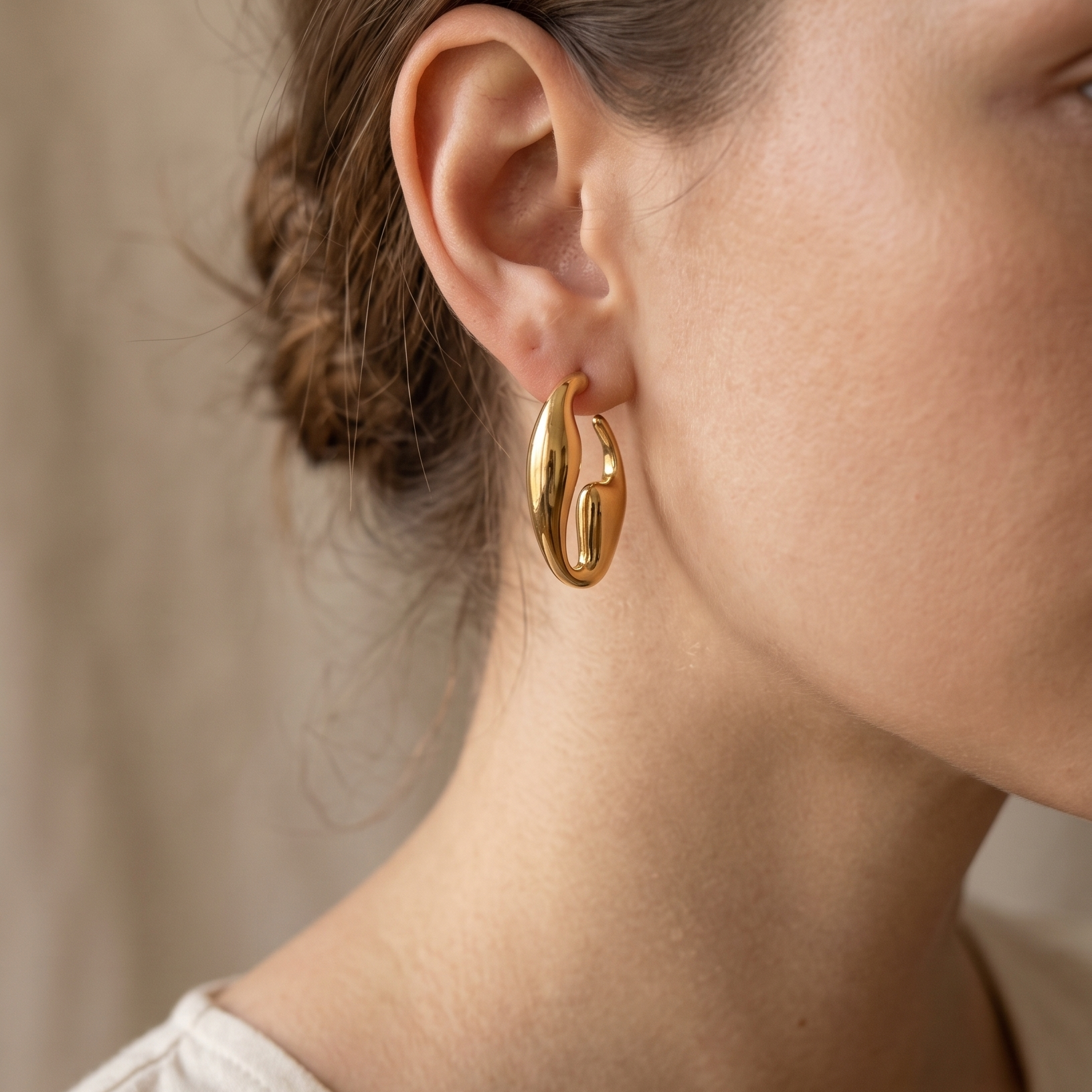 Gold hoop earrings worn by a person with a neutral background