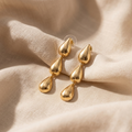 Gold teardrop earrings on a beige fabric background
