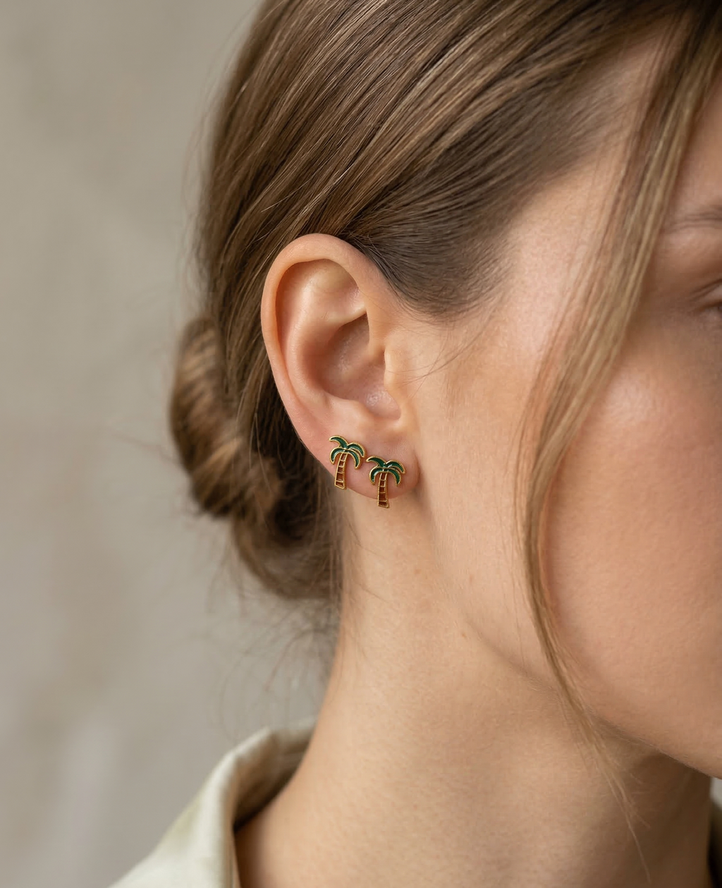 Close-up of a person wearing palm tree earrings with a neutral background