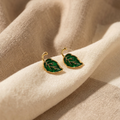 Green leaf-shaped earrings on a beige fabric background