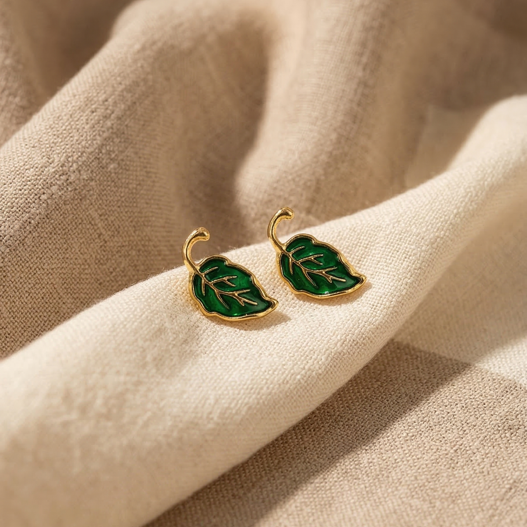 Green leaf-shaped earrings on a beige fabric background