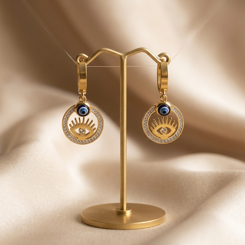Gold earrings on a matching stand against a beige fabric background