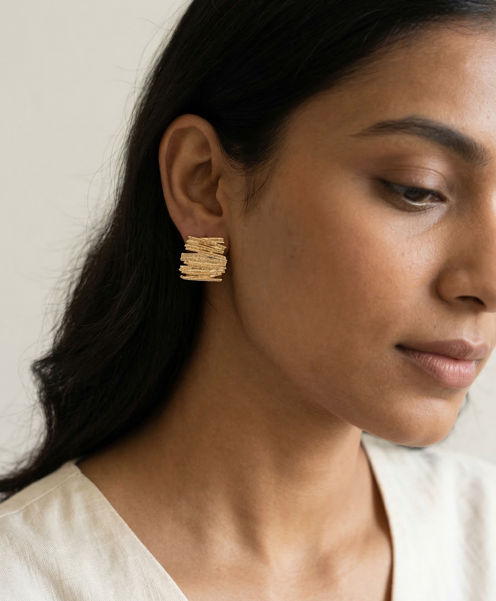 Close-up of a woman wearing gold hoop earrings against a neutral background