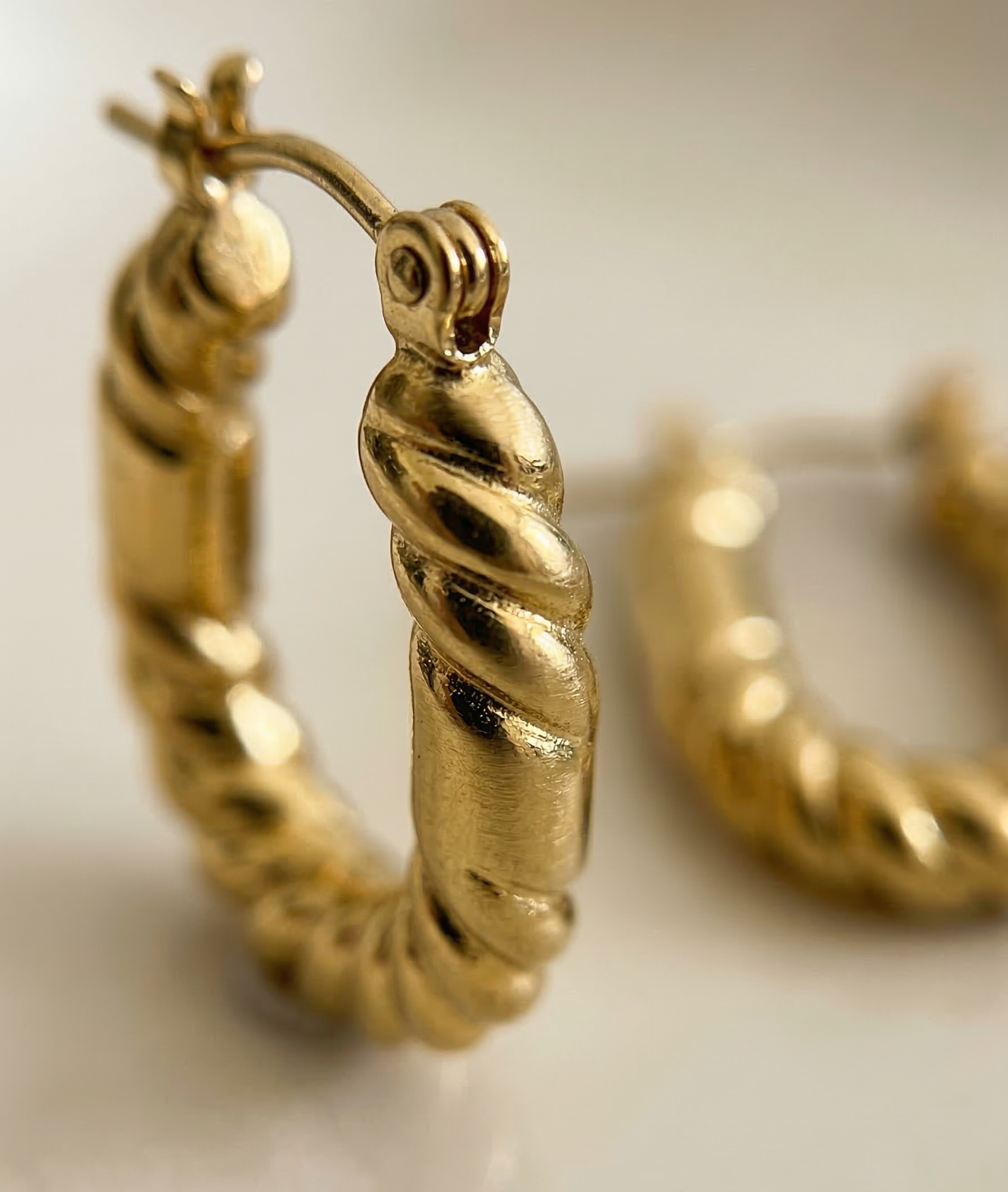 Gold hoop earrings with twisted design on a light background