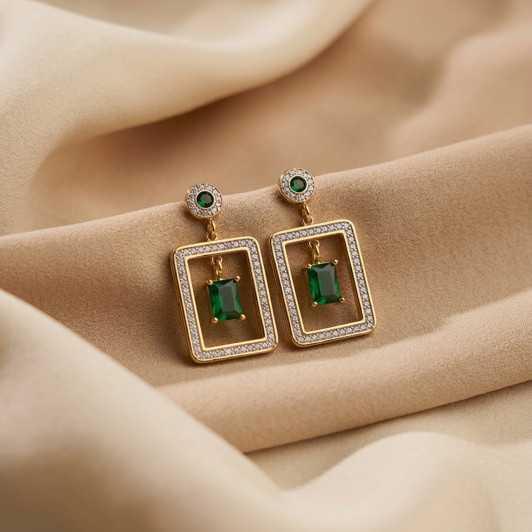 Pair of gold earrings with green gemstones on beige fabric