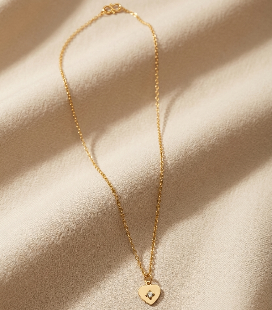 Gold necklace with a heart-shaped pendant on a beige fabric background