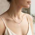 Woman wearing a delicate gold necklace against a neutral background