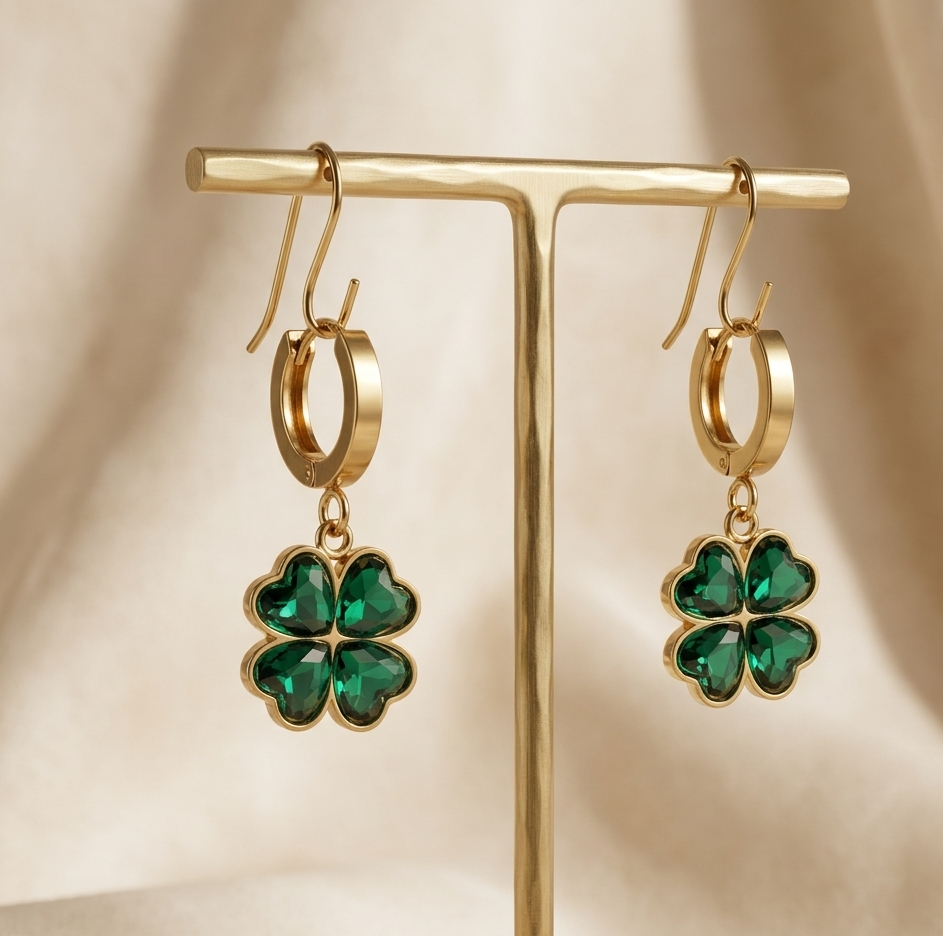 Gold earrings with green gemstones on a gold stand against a beige background