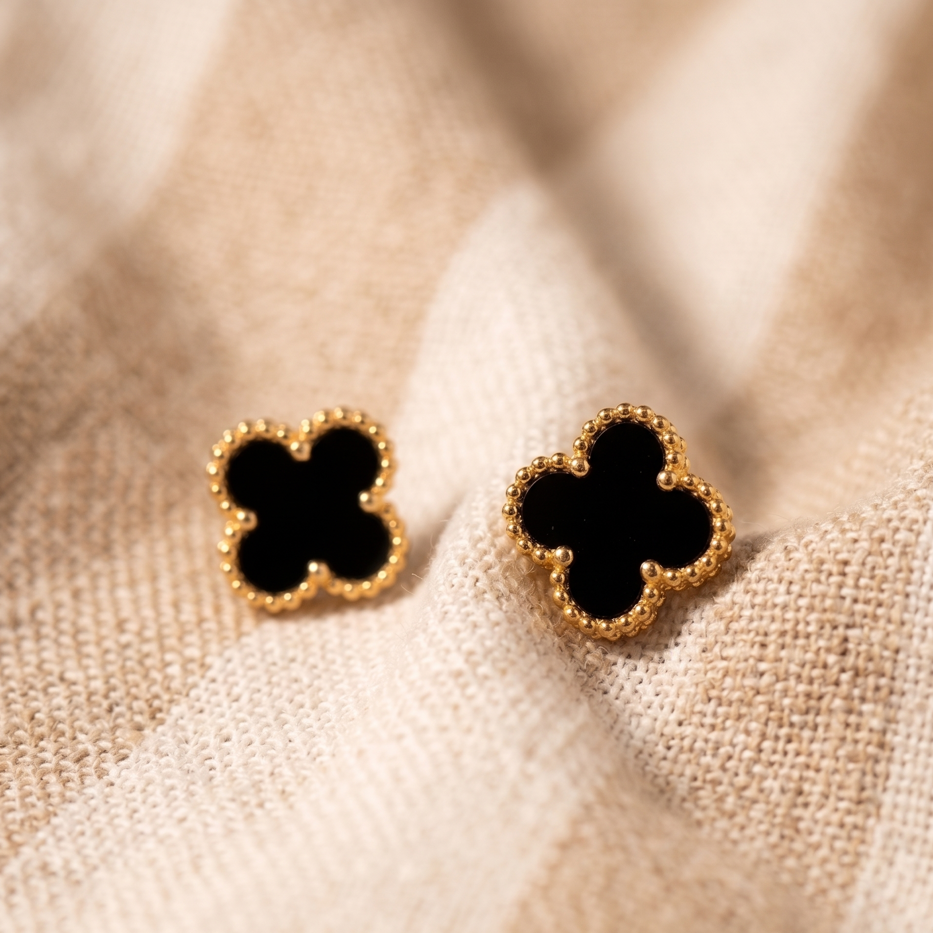 Pair of gold and black clover-shaped earrings on a beige fabric background