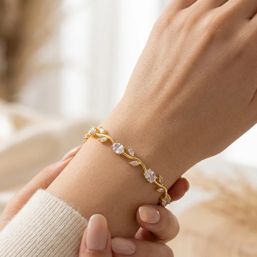 A delicate gold vine bracelet with clear crystal leaves, shown worn on a woman's wrist with her hands gently holding it.