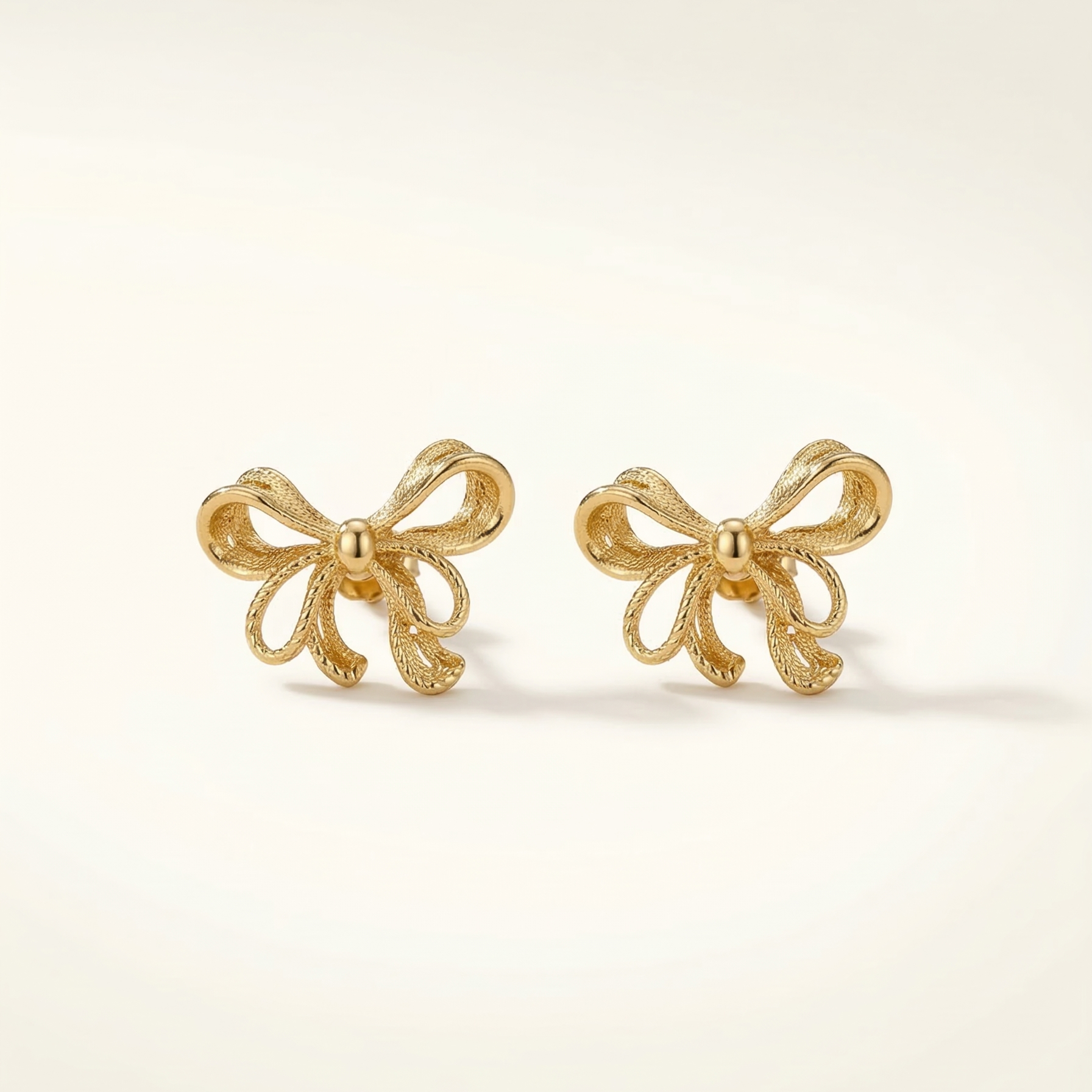 Gold bow-shaped earrings on a light beige background