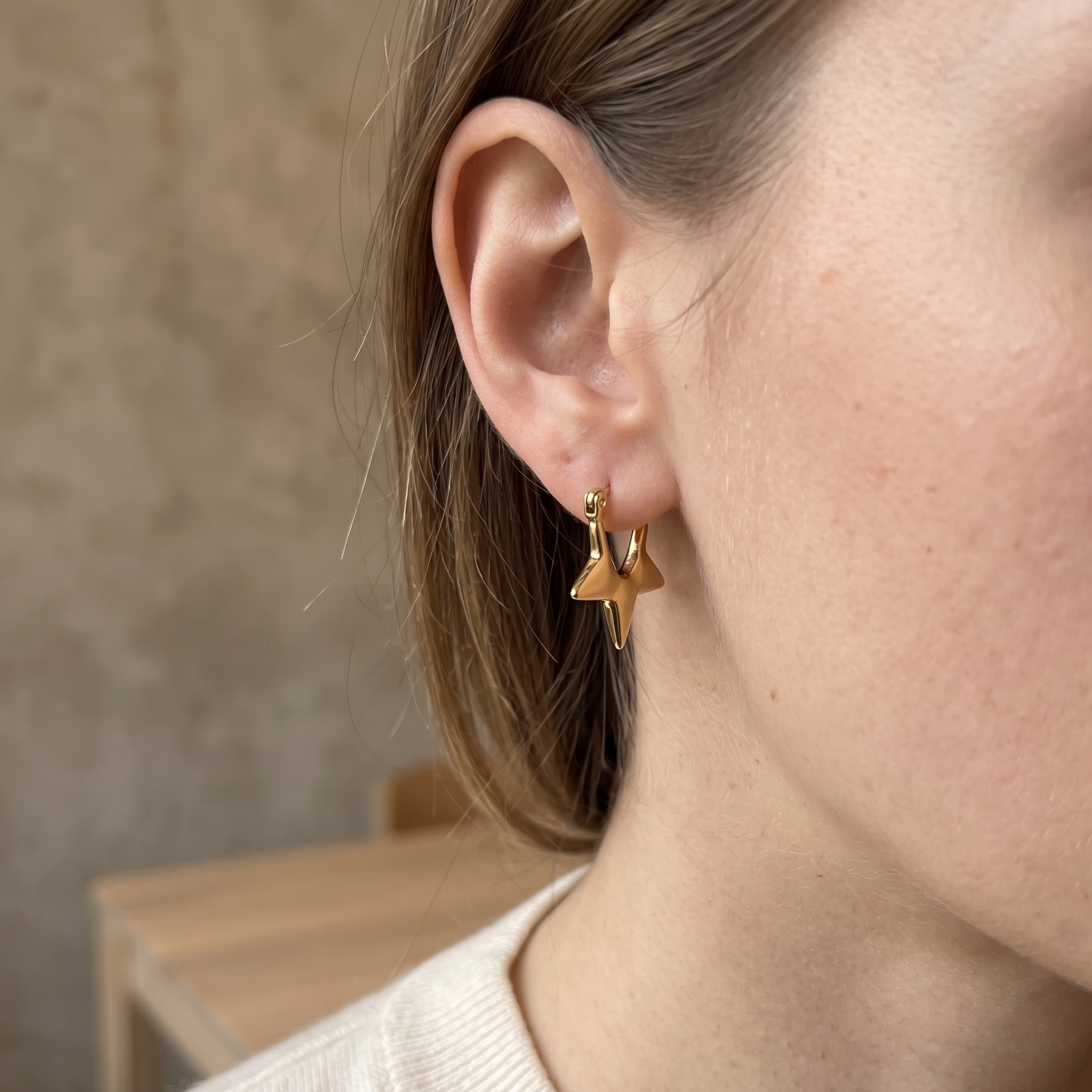 Close-up of a person wearing gold star-shaped earrings with a neutral background