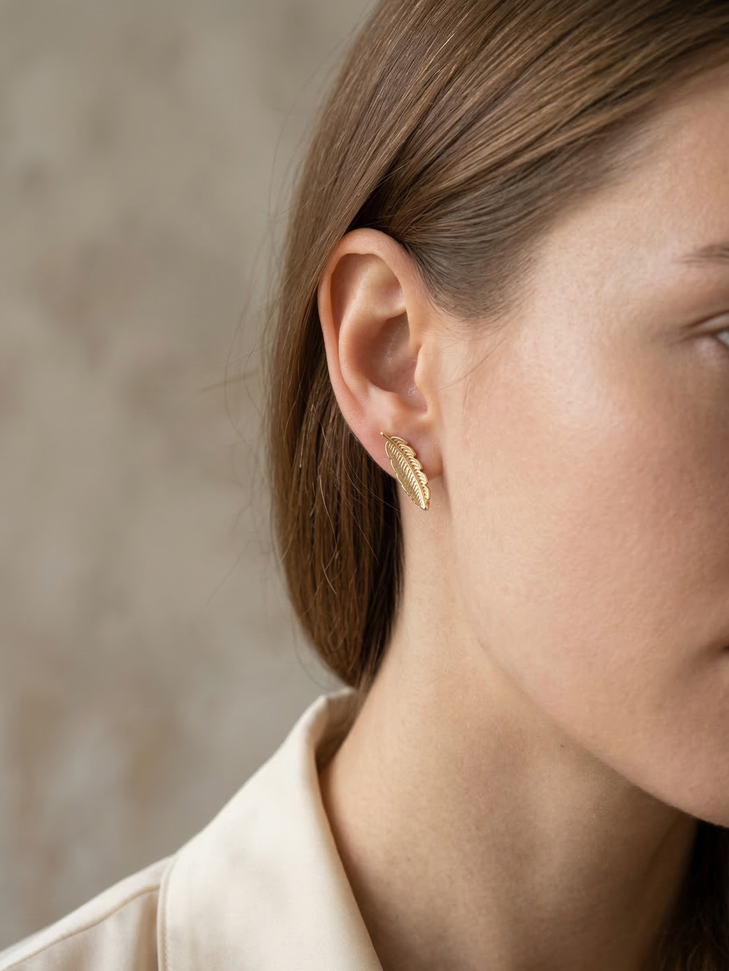 Close-up of a person wearing a gold earring with a neutral background