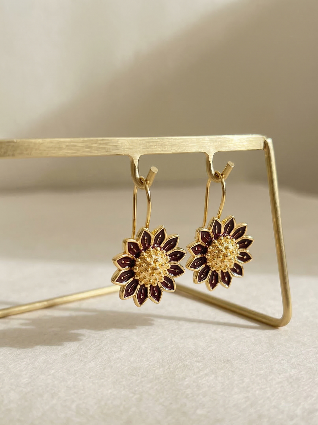 Gold and red floral earrings on a gold stand against a beige background