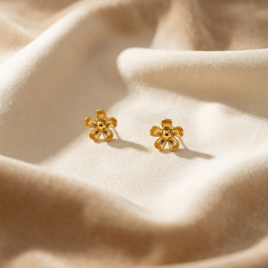 Pair of gold flower-shaped earrings on beige fabric