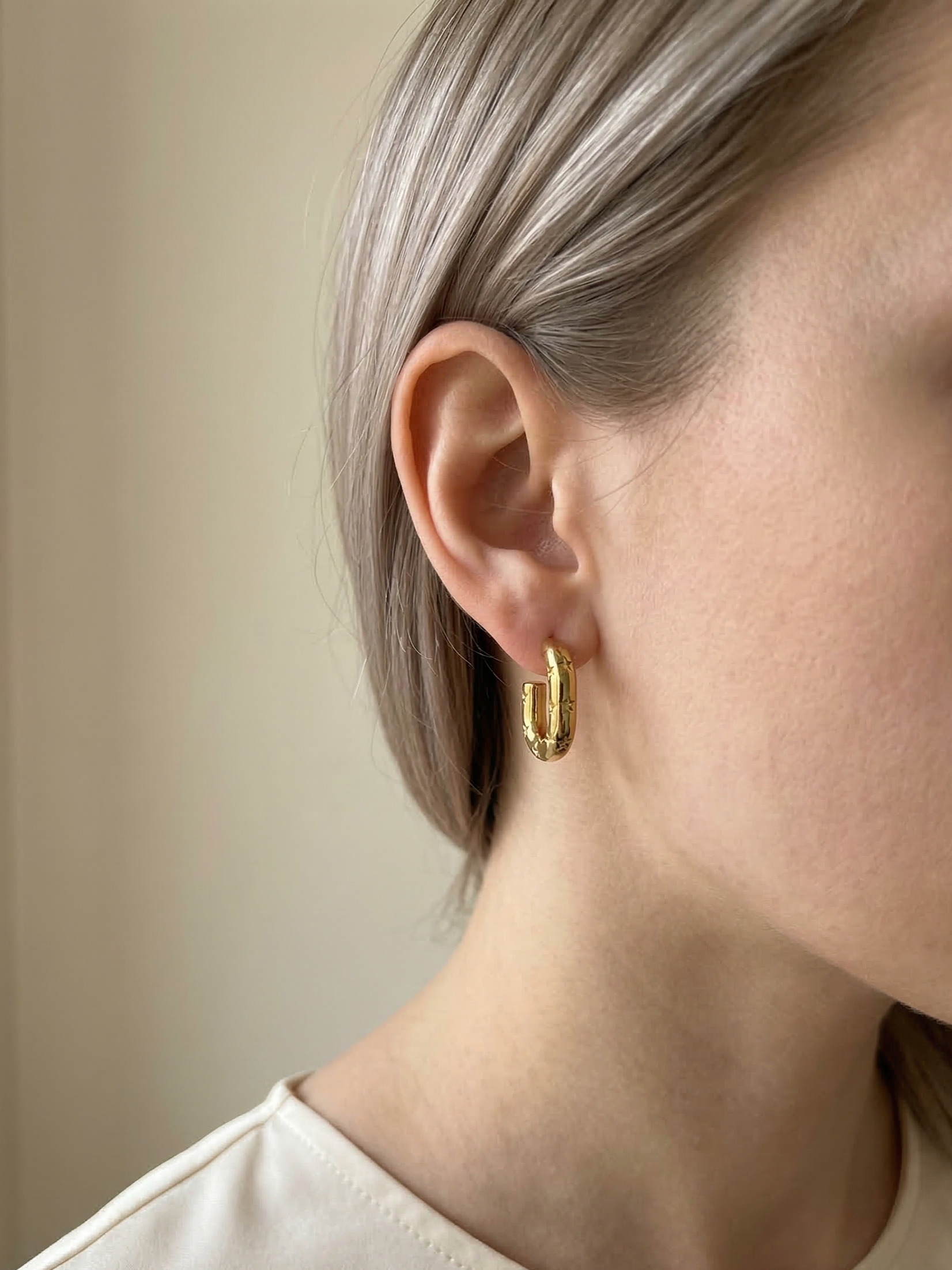 Close-up of a person wearing gold hoop earrings with a neutral background