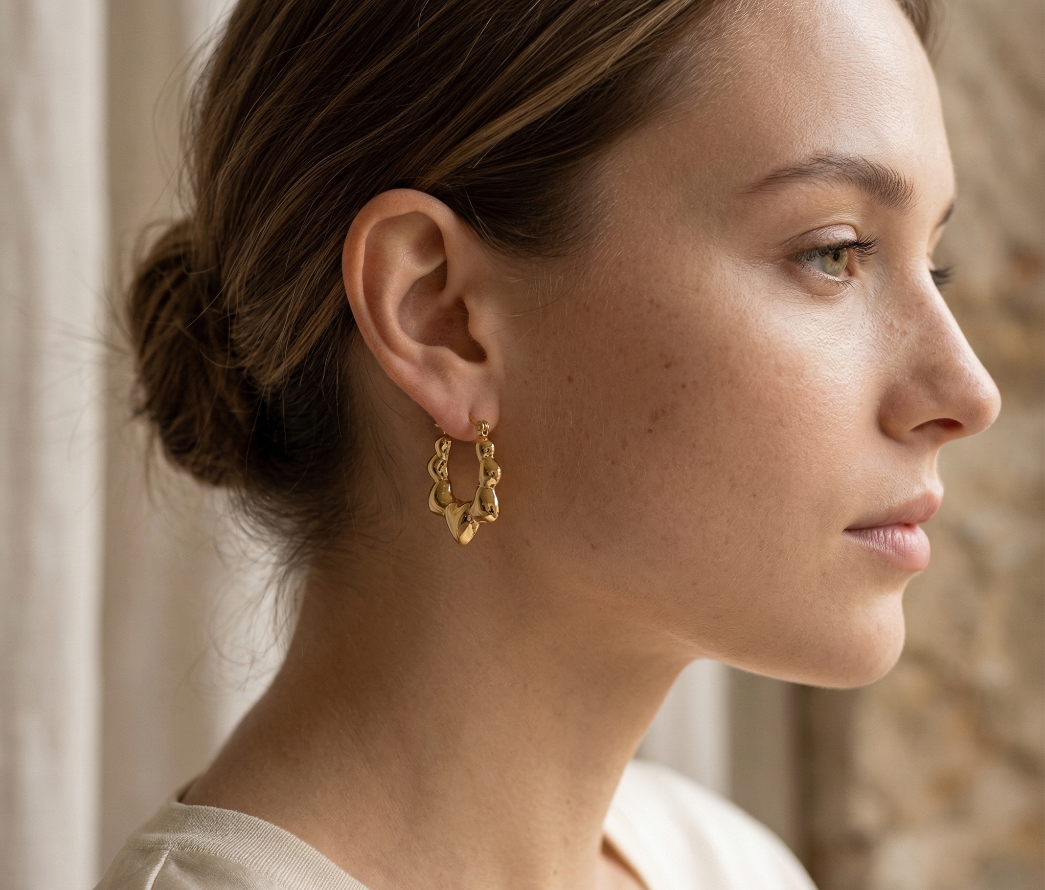 Close-up of a woman wearing gold earrings with a neutral background