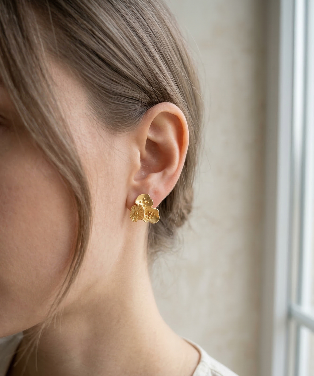 Gold earrings worn by a person with a neutral background