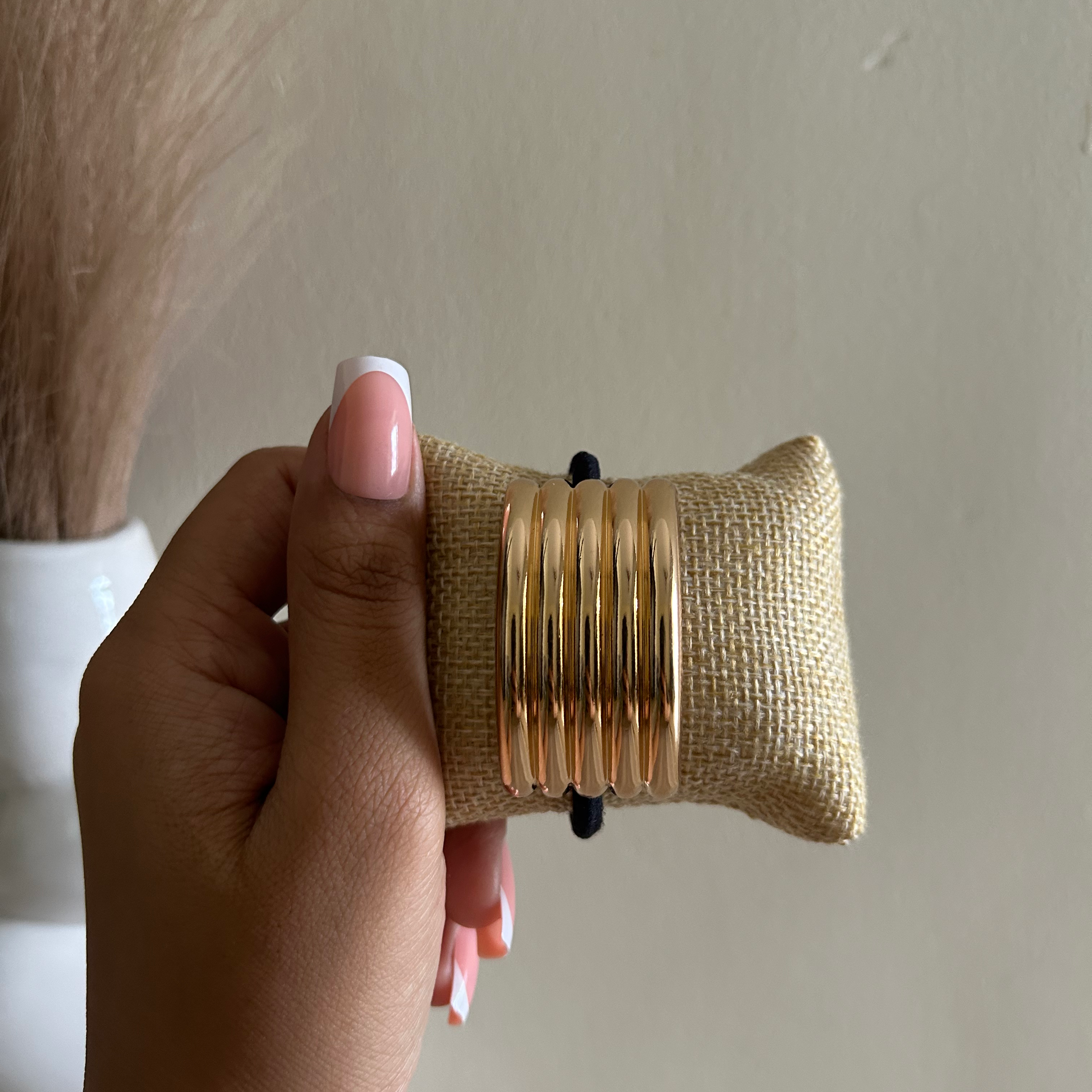 Hand holding a gold bracelet on a burlap cushion with a neutral background