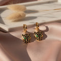 Gold panther head earrings with green and black accents on a pink fabric background