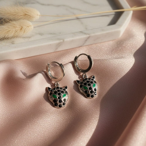 Pair of silver earrings with green gemstones on a pink fabric background