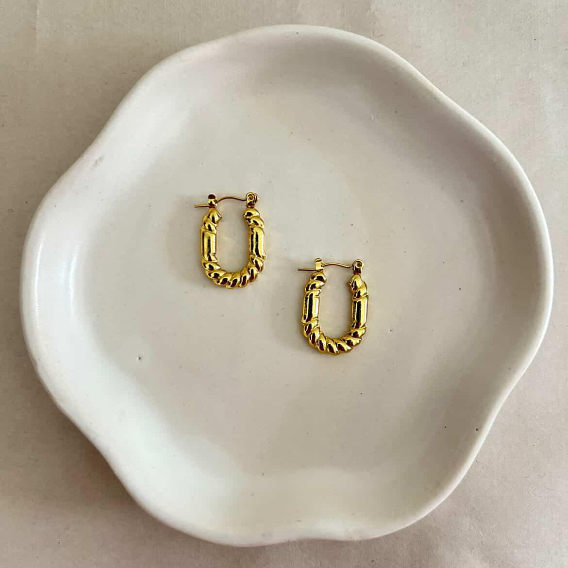 Gold hoop earrings on a white ceramic dish with a plain background