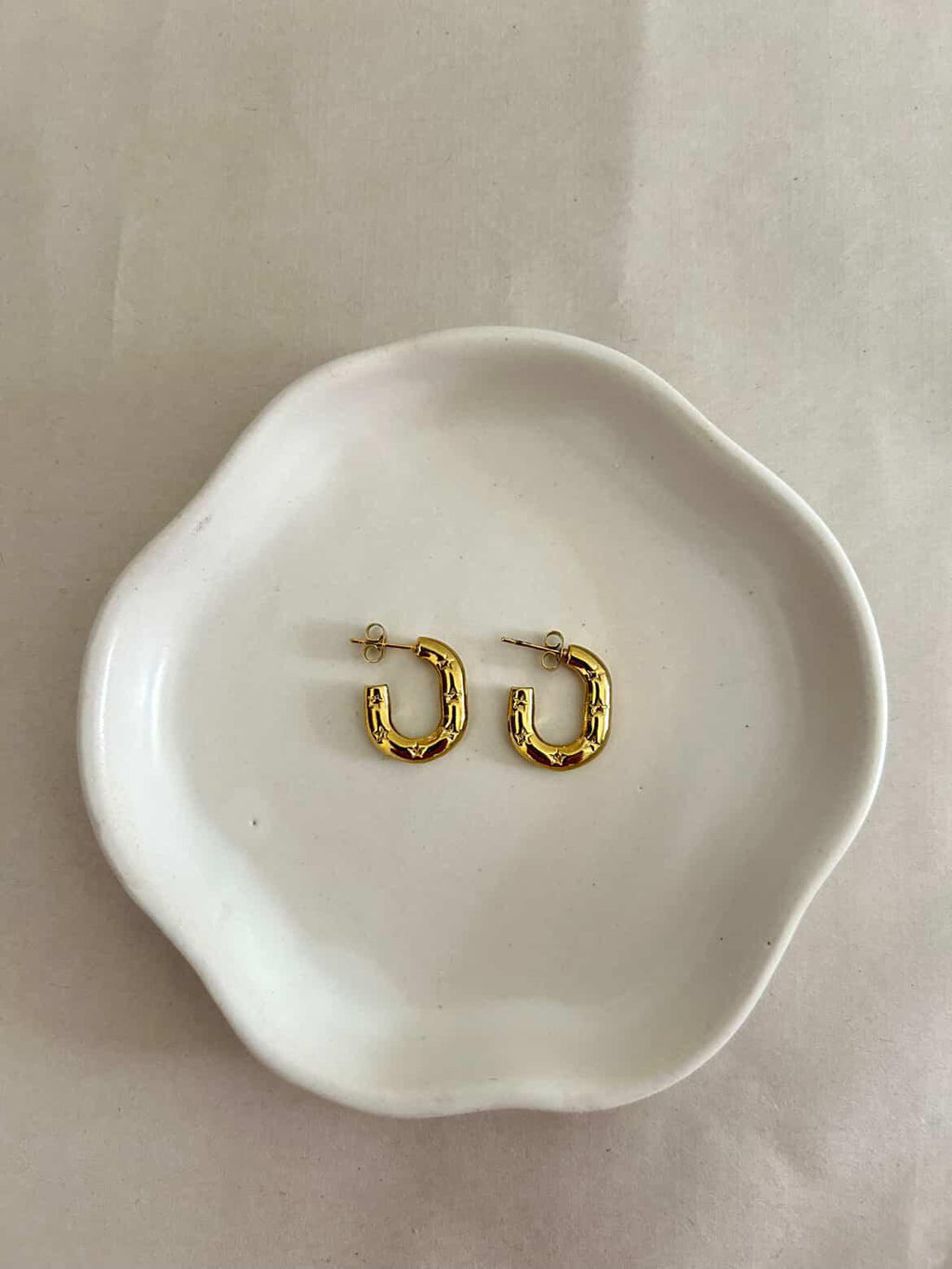 Gold hoop earrings on a white ceramic dish with a plain background