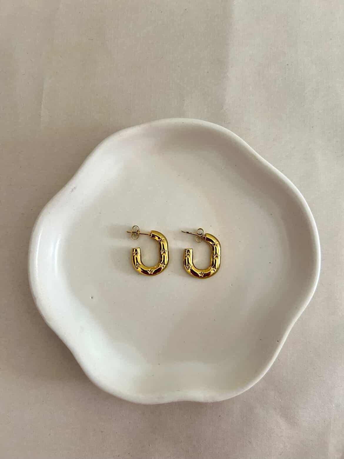 Gold hoop earrings on a white ceramic dish with a plain background