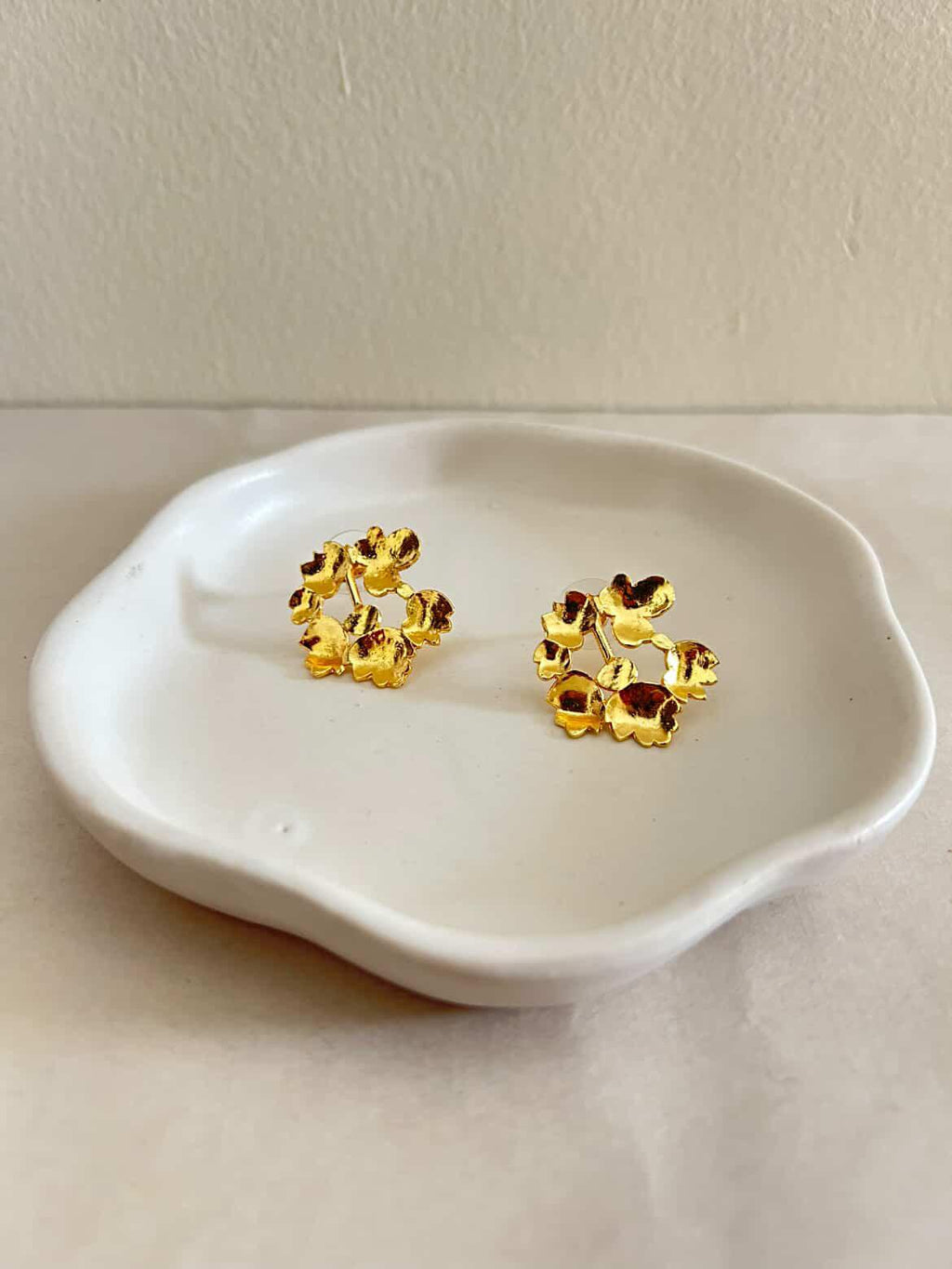 Gold earrings with red stones on a white dish against a beige background