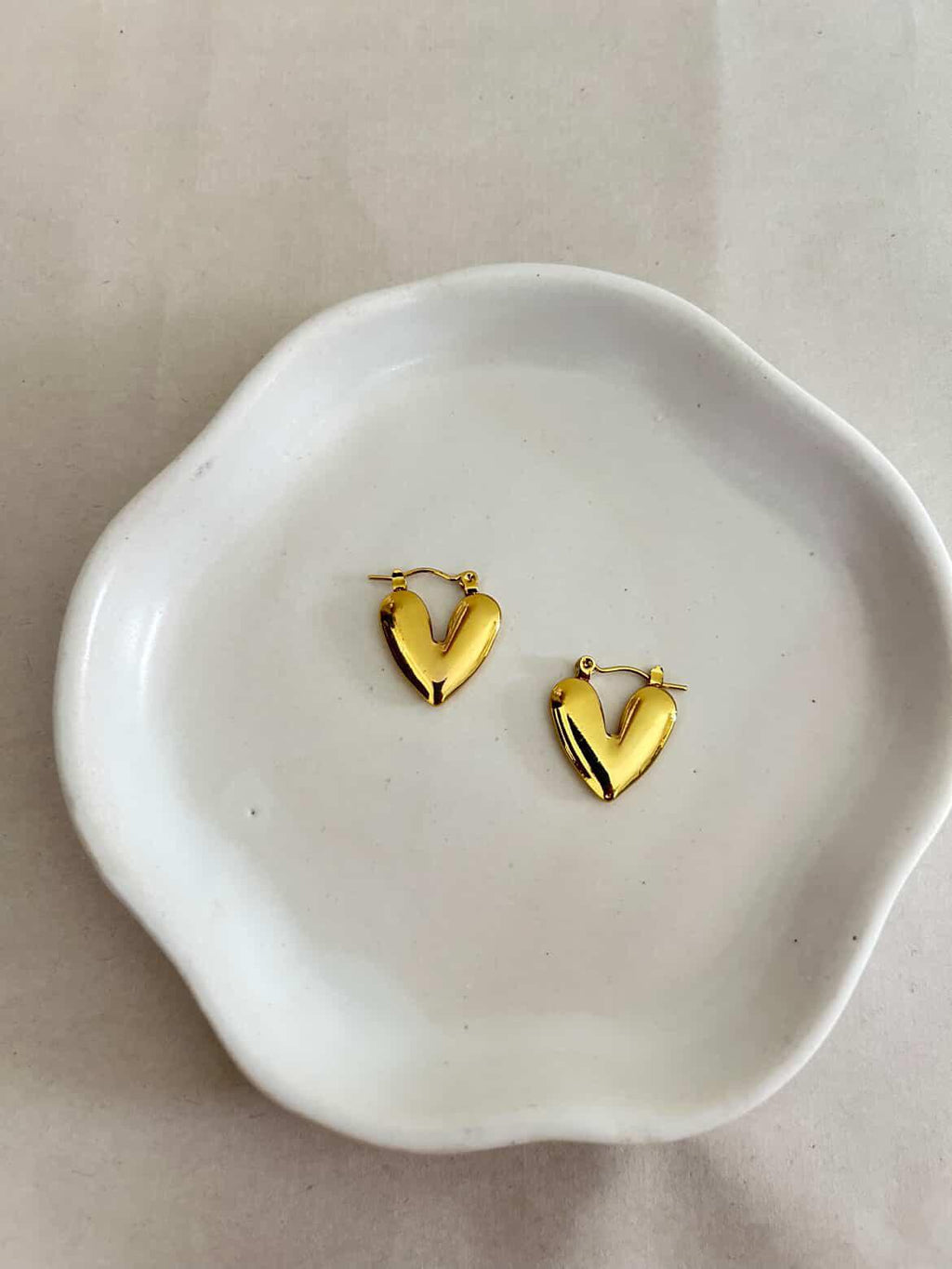 Gold heart-shaped earrings on a white ceramic dish
