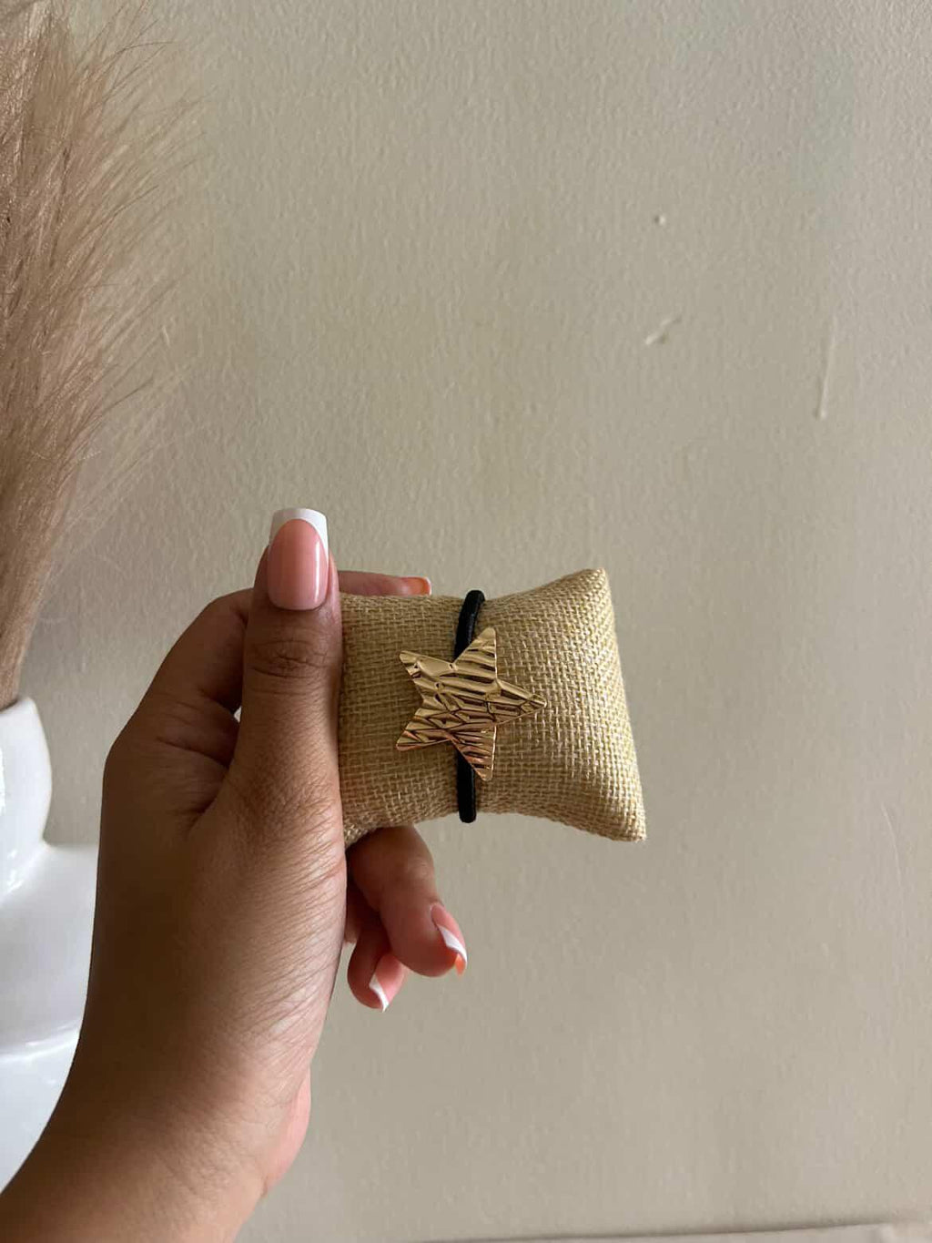 Hand holding a small brown fabric pouch with a black cord against a plain background