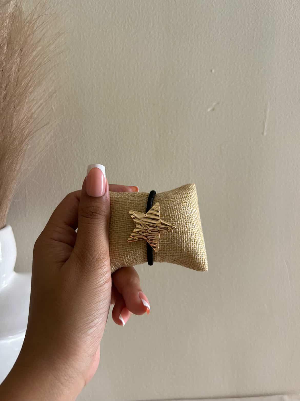 Hand holding a small brown fabric pouch with a black cord against a plain background