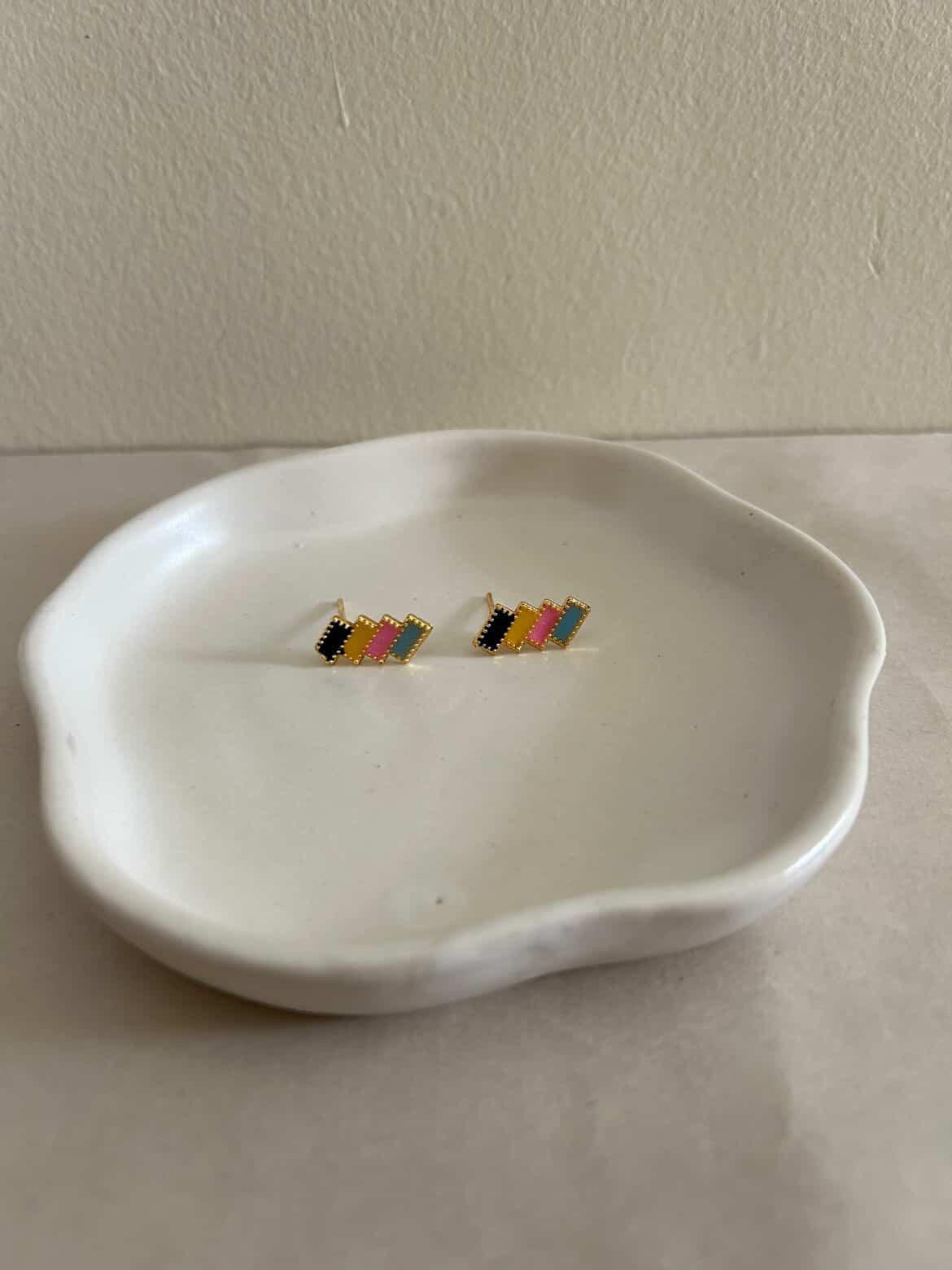 Colorful geometric earrings on a white dish against a plain background