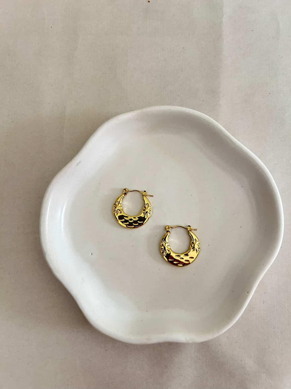 Gold hoop earrings on a white ceramic dish against a light background