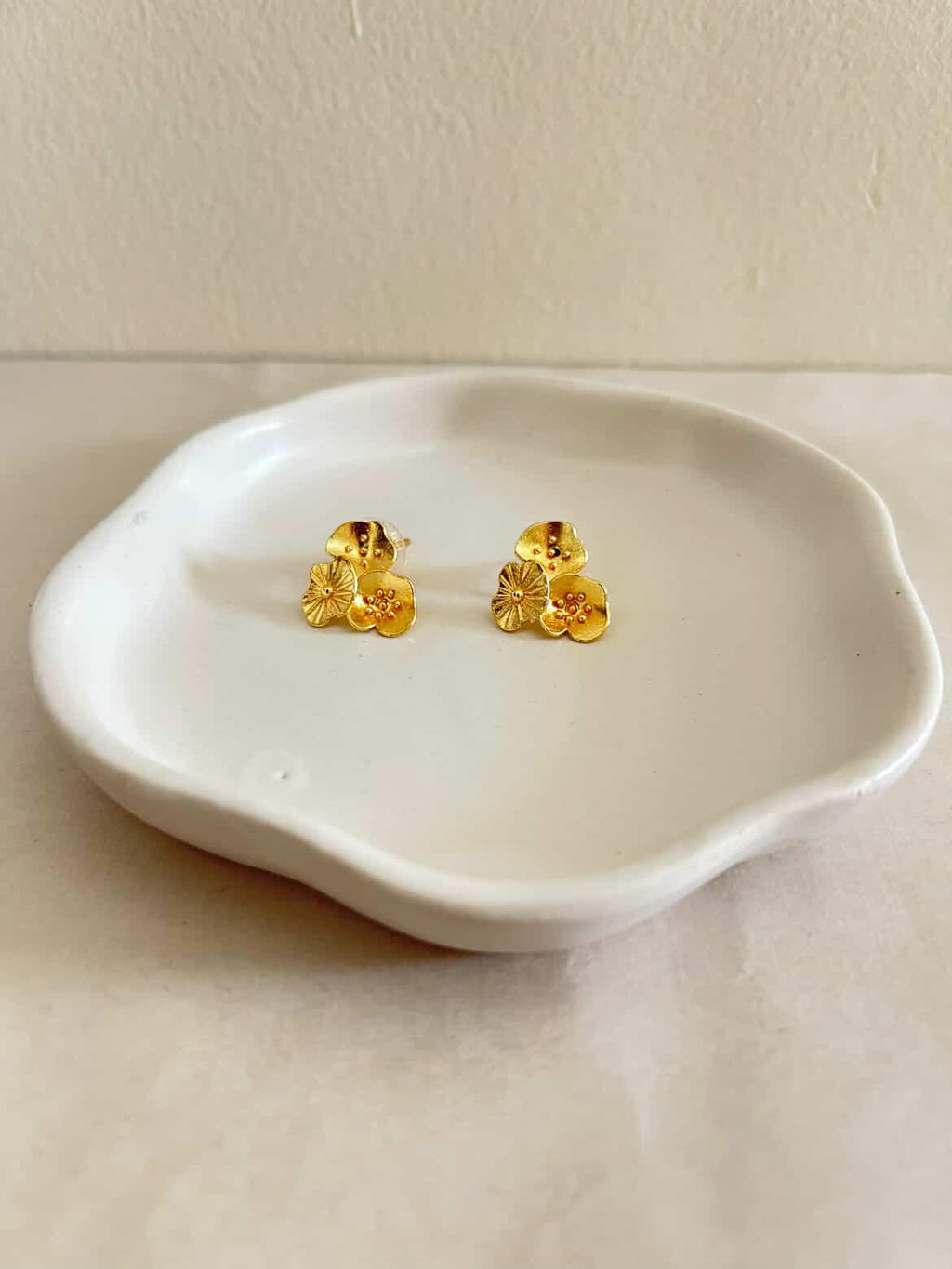Gold floral earrings on a white ceramic dish against a light background