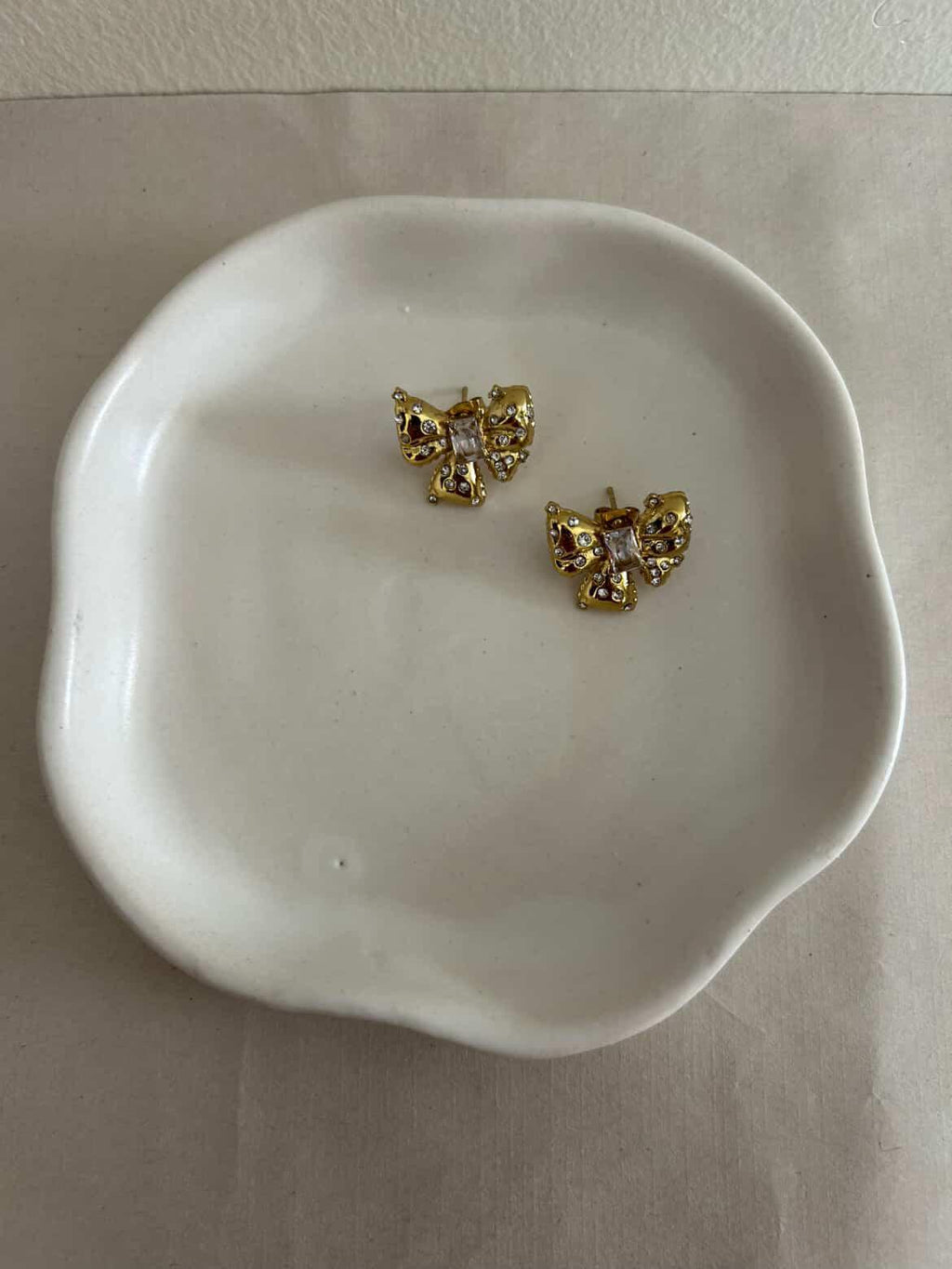 Gold earrings with gemstones on a white dish.