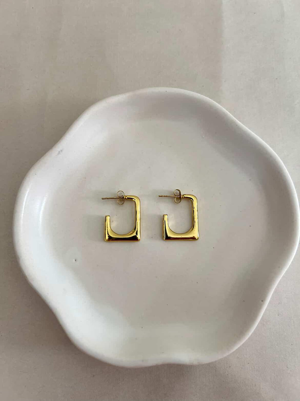 Gold hoop earrings on a white dish with a plain background