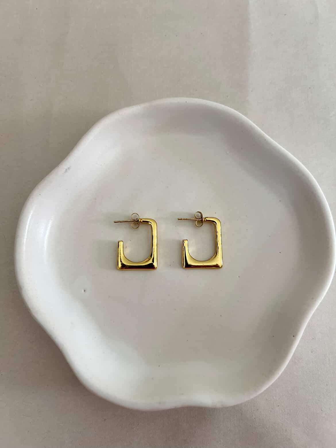Gold hoop earrings on a white dish with a plain background