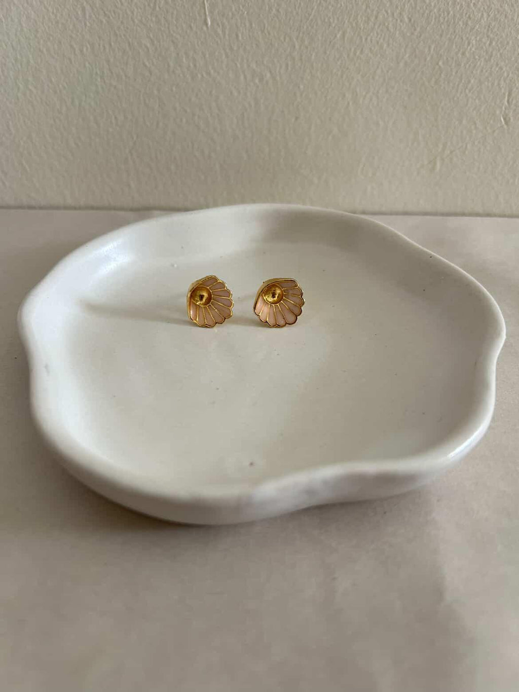Gold earrings on a white ceramic dish against a plain background