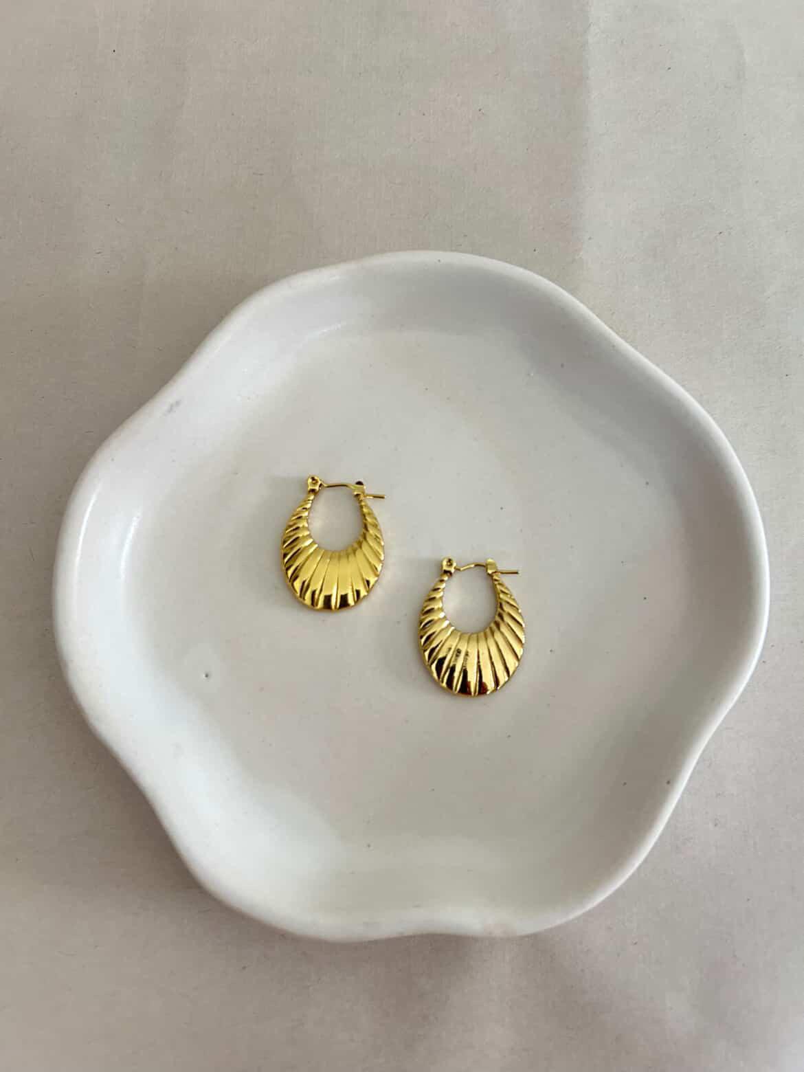 Gold hoop earrings on a white ceramic dish with a plain background