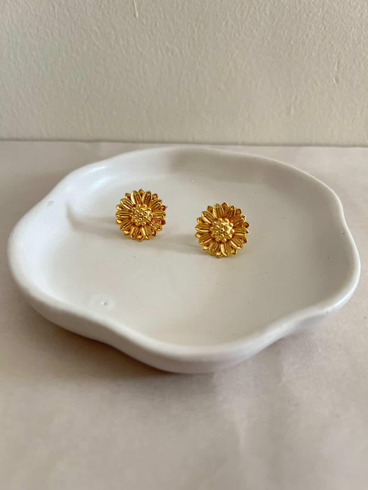 Gold floral earrings on a white dish against a white background