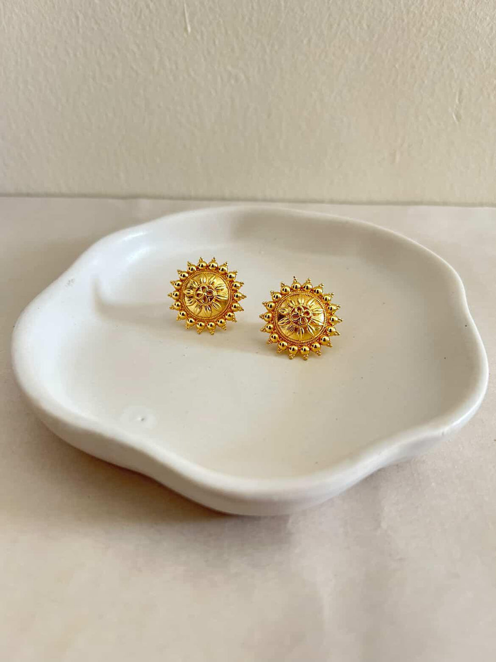 Gold earrings on a white ceramic dish against a light background