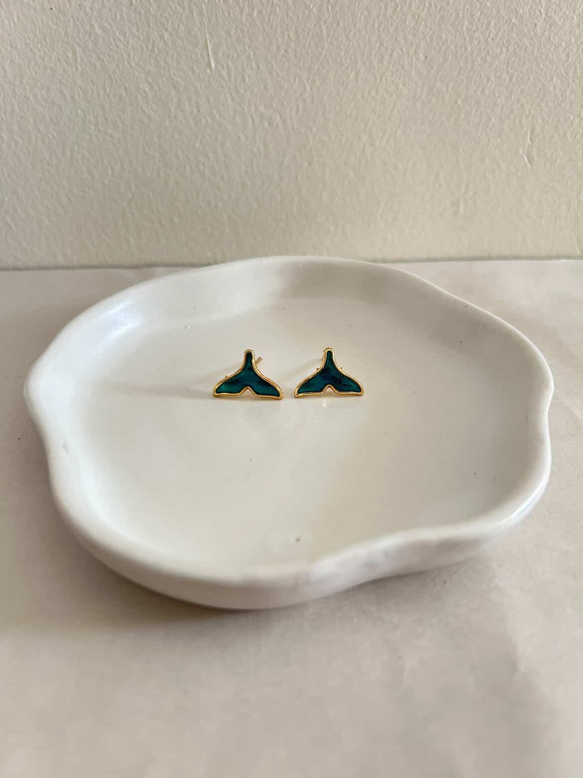 Pair of green and gold earrings on a white dish against a beige background