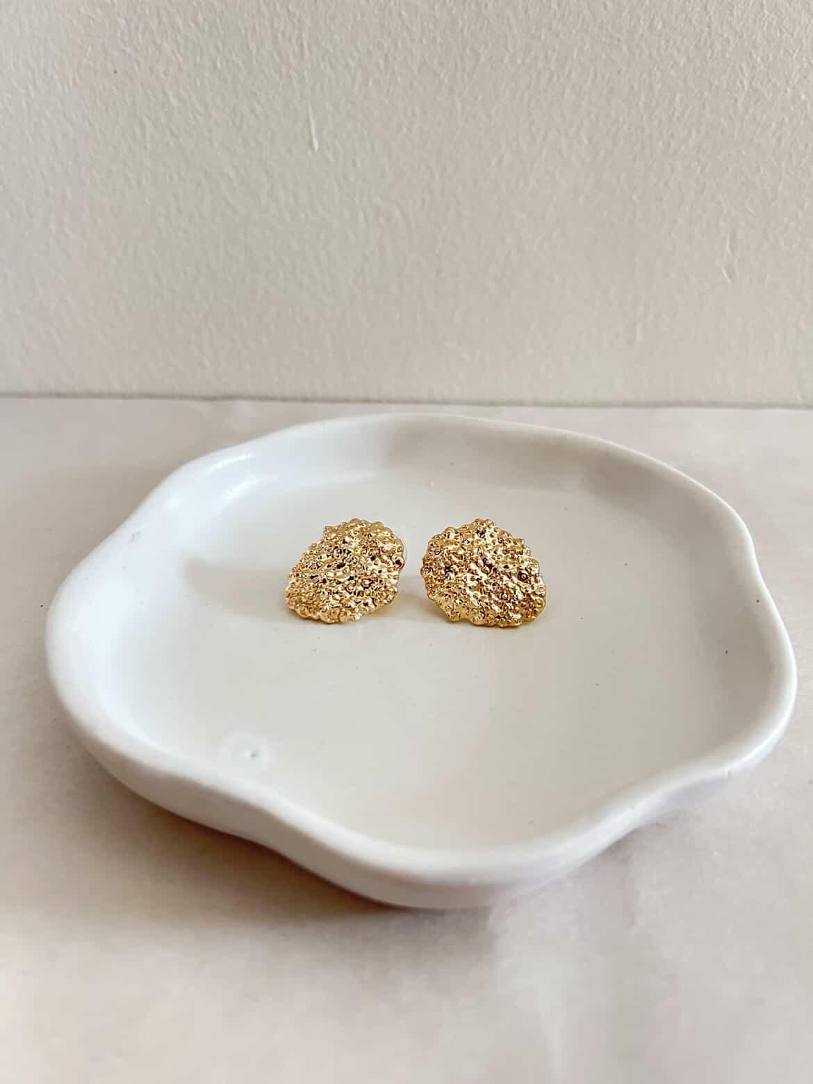 Gold earrings on a white ceramic dish against a plain background