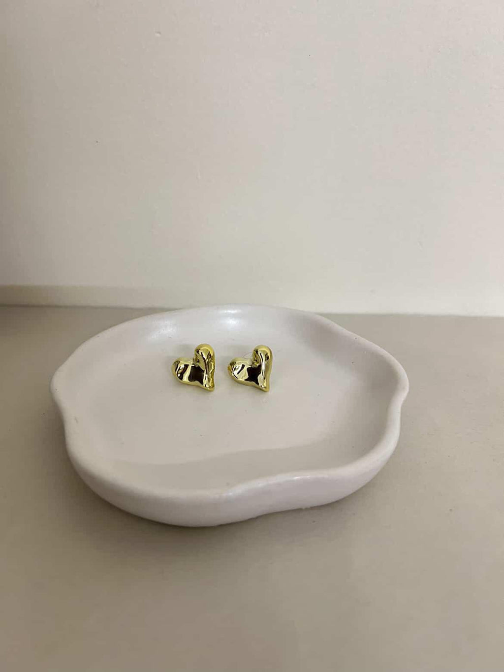 Gold heart-shaped earrings on a white dish with a plain background
