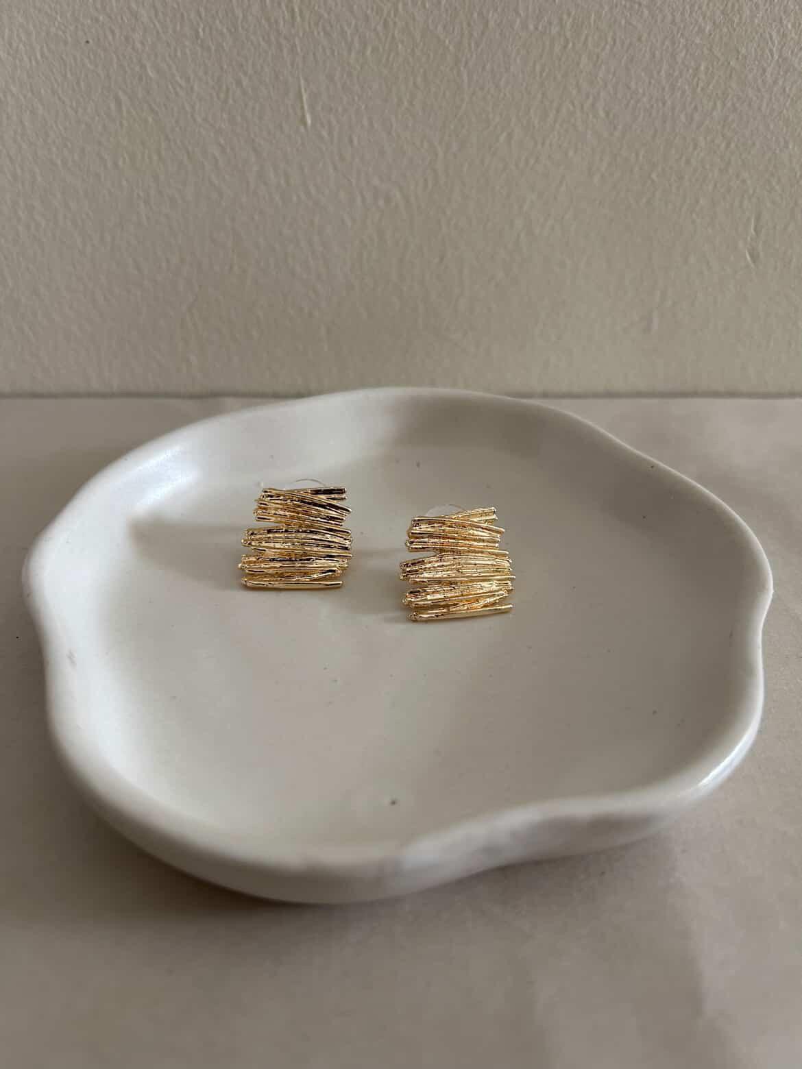 Gold earrings on a white dish against a plain background